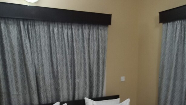 Quarto de hotel com cama bem arrumada, cabeceira e cortinas cinzas.