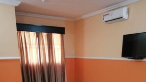 Uma sala de estar com sofás laranja, uma mesa de centro de madeira e uma televisão na parede.