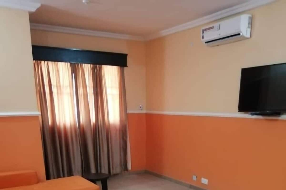 A living room with orange sofas, a wooden coffee table, and a television on the wall.