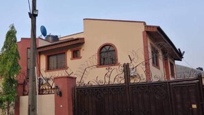 Uma casa de dois andares com fachada bege, um portão marrom escuro e uma antena parabólica.