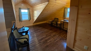Une chambre mansardée chaleureuse avec des murs en bois, un plafond en pente, une petite table avec des chaises et une fenêtre offrant une belle vue.