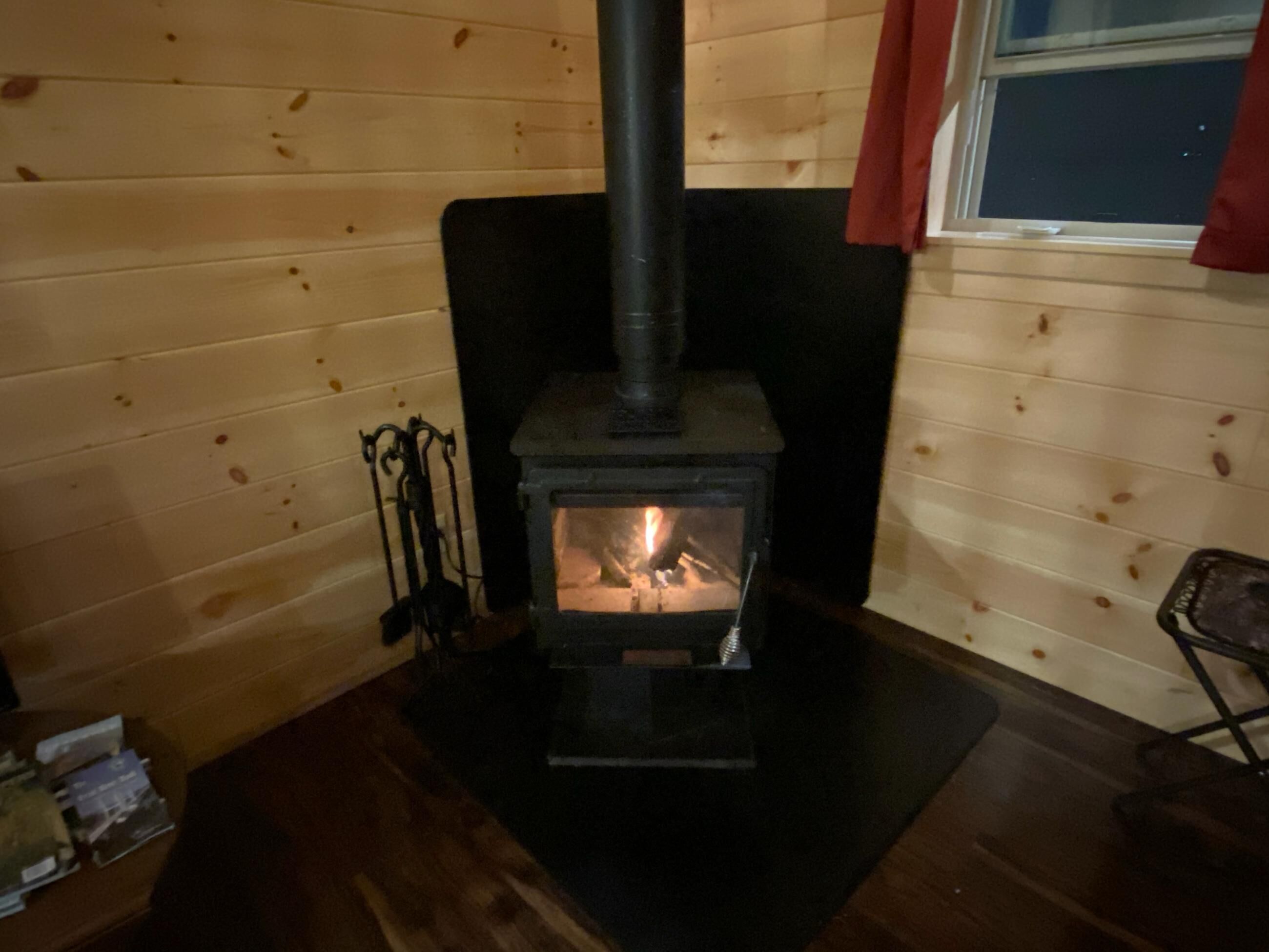 Een houtkachel in een kamer met houten wanden en een raam.