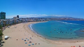 Eine Küstenstadtlandschaft mit einem weiten Sandstrand, klarem, blauem Wasser und einer Mischung aus modernen und traditionellen Gebäuden.