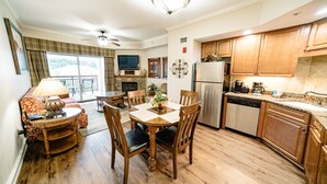 A dining area with a wooden table and chairs, a fireplace, and a kitchen with wooden cabinets and a refrigerator.