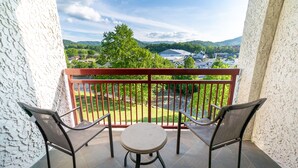 A balcony with two chairs and a small table, overlooking a green landscape and buildings.