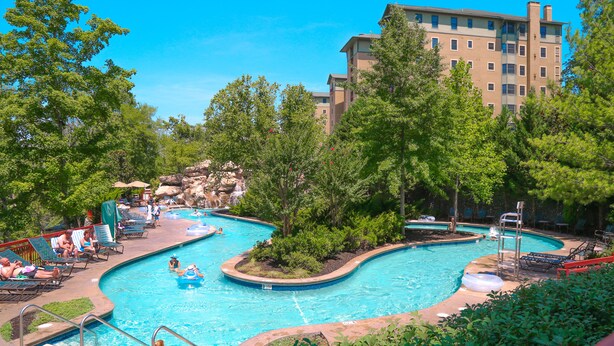A swimming pool with multiple lanes, surrounded by trees and lounge chairs.
