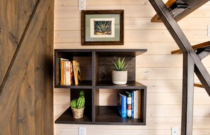 A wooden wall with a black metal staircase, a framed picture, and a shelf with books and plants.