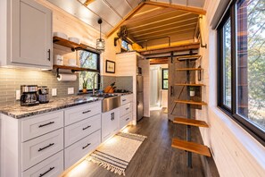 A modern kitchen with white cabinets, a marble countertop, and a wooden ceiling. - La Petite: a Tiny House Tucked in Nature *Hot Tub* (Hays County)