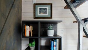 Una estantería con libros, una planta en maceta y un cuadro en la pared.