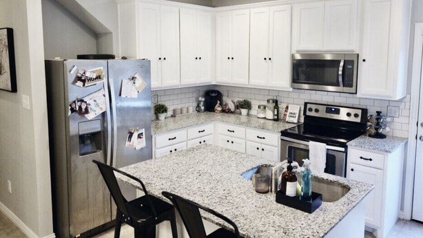 A kitchen with white cabinets, a granite countertop, a refrigerator, a microwave, an oven, and a sink. - Spacious Modern Retreat House (Garland)