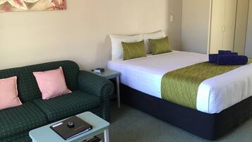 Een hotelkamer met een groene bank, een bed met wit en groen beddengoed, een klein tafeltje met een laptop en boeken, en een schilderij aan de muur.