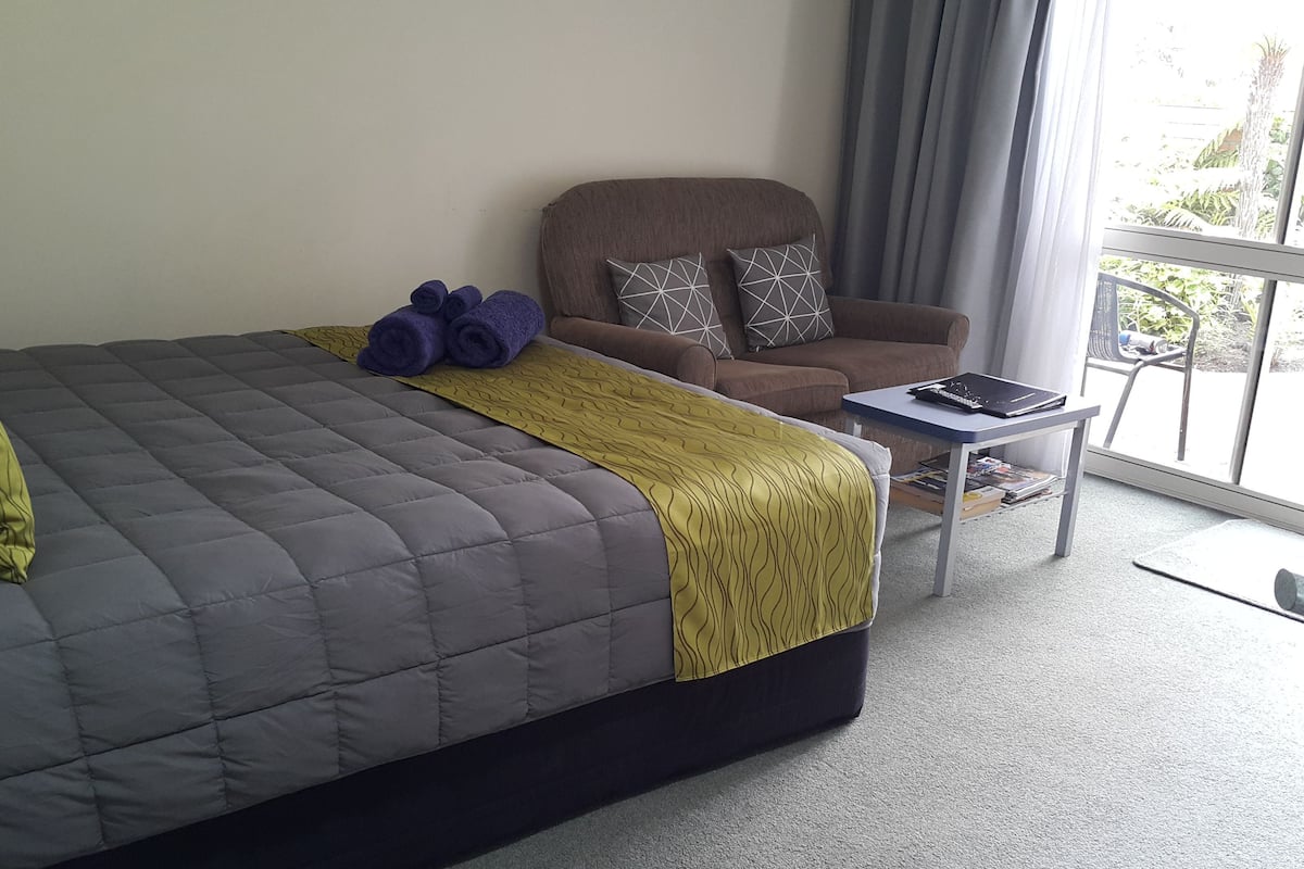 Ein Schlafzimmer mit einem großen Bett, einem Sessel, einem kleinen Tisch und Blick ins Freie.