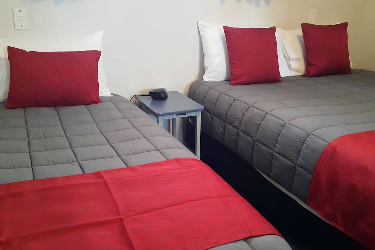 Ein Zimmer mit zwei Betten, jedes mit einem roten und weißen Kopfkissen, und einem kleinen Tisch mit einem schwarzen Gegenstand darauf.