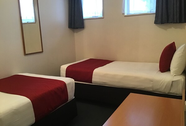 A room with two single beds, each with a red and white bedspread, and a wooden table in the foreground.