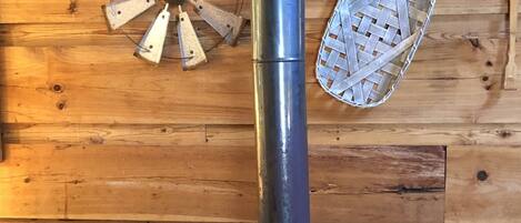 A wood stove with a metal chimney, a woven basket, and a woven wall decoration.