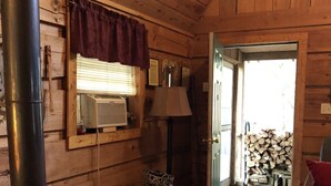 Ein gemütliches Blockhaus-Interieur mit Kaminofen, einer Bank, einer Lampe und einer Tür, die nach draußen führt.