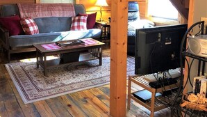 Ein gemütliches Blockhaus-Interieur mit Holzbalkendecke, einer Sofagarnitur, einem Couchtisch, einem Fernseher und einem Kamin.