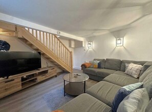 A modern living room with a wooden staircase, a flat-screen TV on a wooden stand, a grey sofa, and a round coffee table. - West Lodge, Filey. Sleeps 8. 5minutes to beach (Filey)