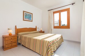 A bedroom with a bed, wooden nightstands, a lamp, a painting, and a window with curtains. - Voramar 2F - Nice apartment with communal pool in Port de Pollença (Port de Pollença)