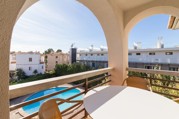 A balcony with a pool, wicker chairs, and a table. - Voramar 2F - Nice apartment with communal pool in Port de Pollença (Port de Pollença)