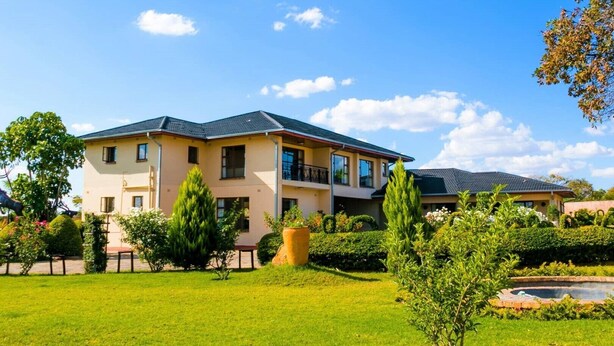 A two-story residential building with a flat roof, multiple balconies, and a well-maintained garden with a small pond. - Bhimi Getaway Guest House (Burnside Bulawayo)