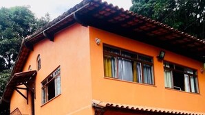 A two-story building with a staircase leading to the entrance, a tiled roof, and a paved courtyard. - Chácara Paraíso (Miguel Pereira)