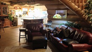 Een gezellige woonkamer met een leren bank, een bijpassende fauteuil en een houten salontafel. Achtergrond toont een keuken met een bar.