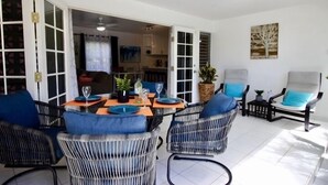 Un espace de vie à aire ouverte comprenant un coin repas avec une table pour quatre personnes, entouré de chaises en osier agrémentées de coussins bleus.