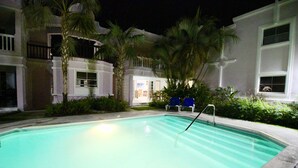 Une piscine la nuit, avec une vue dégagée sur l’espace qui l’entoure, notamment une chaise et une petite structure.