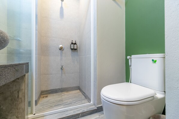 A bathroom with a glass-enclosed shower, a white toilet, and a green wall.