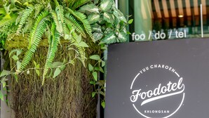 Ein schwarzes Schild mit dem Schriftzug "Foodotel Khlongsan" und eine üppige, grüne Pflanze mit Farnen und anderem Grünzeug.