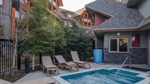 A pool area with lounge chairs and a hot tub, surrounded by wooden buildings and trees. - Spacious 3 BR Top Floor Condo - Kitchen, Mountain View Balcony, Fireplace & Pool (Canmore)