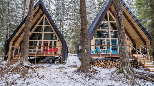 Two wooden cabins with large windows, surrounded by trees and snow. - Salted Roots Red Door A-Frame Cabin (Seward)
