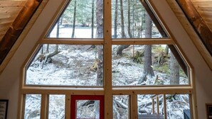 A triangular wooden ceiling with large windows at the base, offering a view of a snowy forest. - Salted Roots Red Door A-Frame Cabin (Seward)