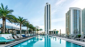 A swimming pool with lounge chairs and palm trees, surrounded by tall buildings.