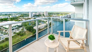 A balcony with a view of a river, a wooden chair, and a small table with a plant.