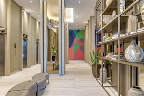 Eine moderne Hotelhalle mit einer zentralen Sitzecke, Aufzügen und einer Wand mit geometrischen Mustern.