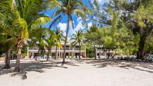 A beachfront hotel with multiple-story buildings, palm trees, and beach chairs. - White Sands 11-Beachfront Condo directly on 7 Mile Beach. Call Cayman Villas! (Seven Mile Beach)