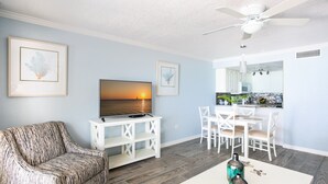 A living room with a sofa, TV, and dining area with chairs and a table. - White Sands 11-Beachfront Condo directly on 7 Mile Beach. Call Cayman Villas! (Seven Mile Beach)