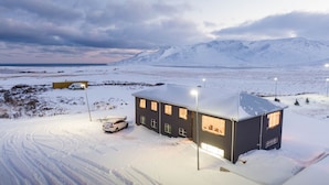 A snow-covered landscape with a building featuring multiple windows and a car parked in front. - Sóti Lodge (Skagafjörour)