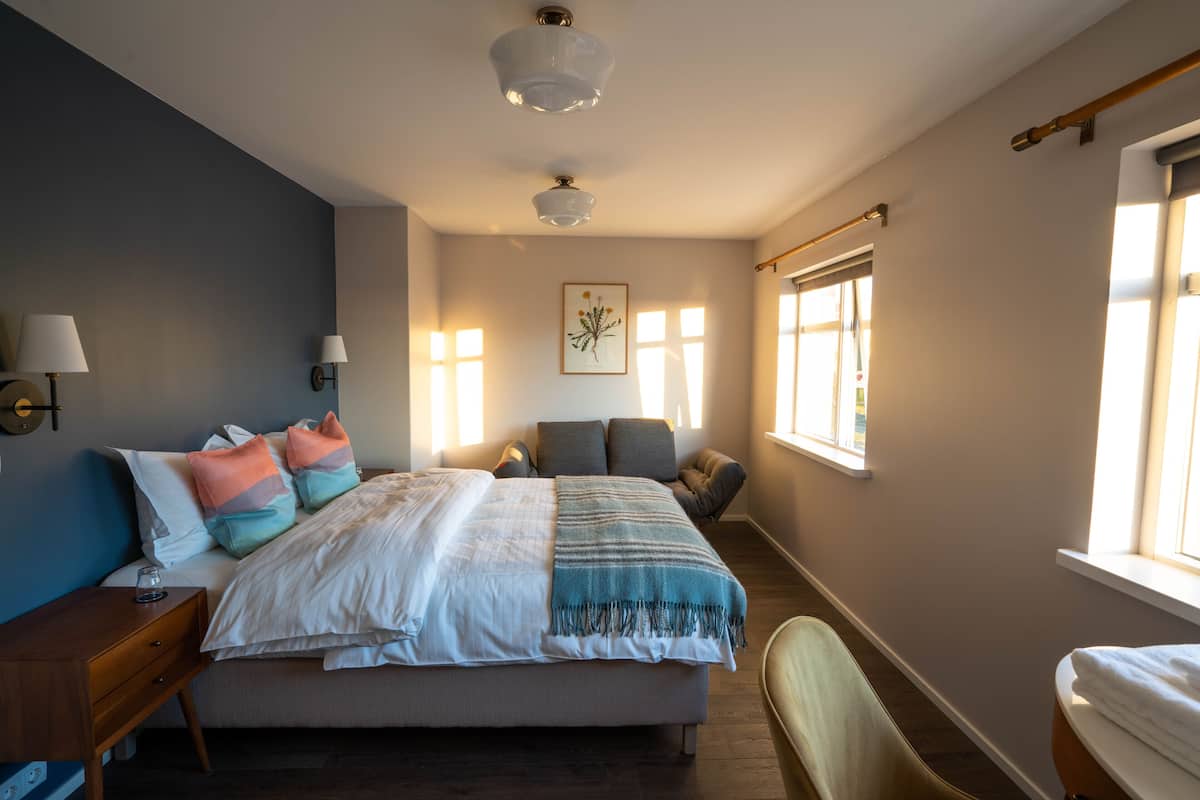 A bedroom with a bed, bedside tables, a chair, a window, and a wall-mounted lamp.