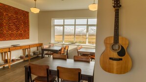 A dining area with a view of mountains, a guitar on the wall, and a patterned rug. - Sóti Lodge (Skagafjörour)