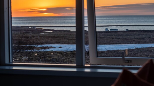 A room with a view of a sunset over the ocean through a window. - Sóti Lodge (Skagafjörour)