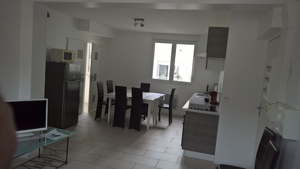 A compact kitchen with a refrigerator, stove, and dining area with chairs and a table. - T4 center LOURDES and near sanctuaries (Lourdes)