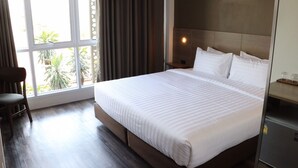 Habitación de hotel con una cama grande, una silla, una mesita de noche y un ventanal con cortinas.