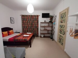 A bedroom with a bed, a TV, a shelf, and a window with curtains. - Cozy Central II Comfortable, welcoming Studio (Ponta Delgada)