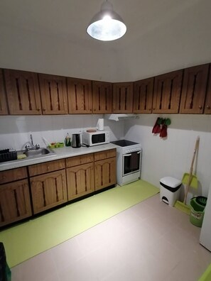 A kitchen with wooden cabinets, a microwave, a stove, a sink, and a broom. - Cozy Central II Comfortable, welcoming Studio (Ponta Delgada)