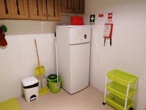 A kitchen with a white refrigerator, a green mop bucket, a yellow broom, a white trash bin, and a green storage rack. - Cozy Central II Comfortable, welcoming Studio (Ponta Delgada)