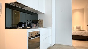 Una cucina moderna con mobili bianchi, forno a incasso e piano cottura. È presente un piccolo angolo ristoro con tavolo e sedie.