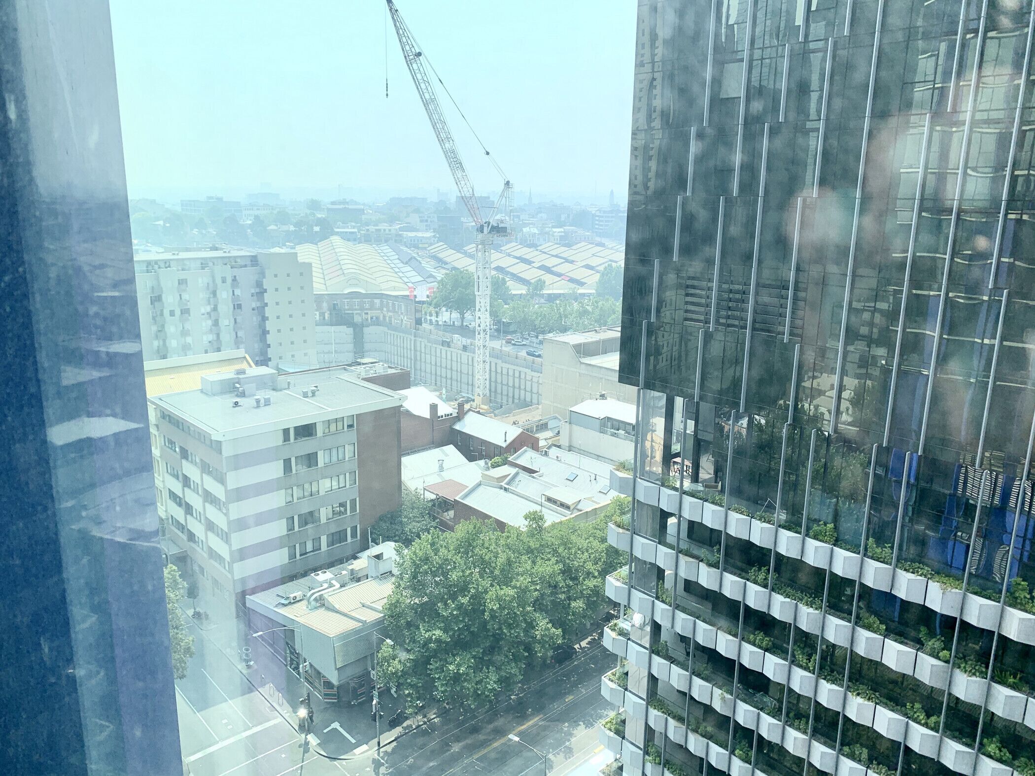 Un edificio de gran altura con fachada de vidrio moderna, rodeado de otros edificios y una grúa de construcción al fondo.